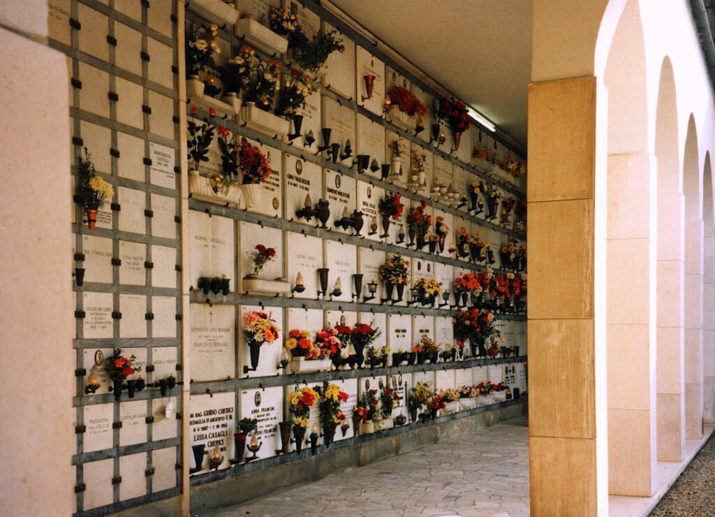 A serene corridor in a Florence cemetery lined with niches adorned with colorful flowers.